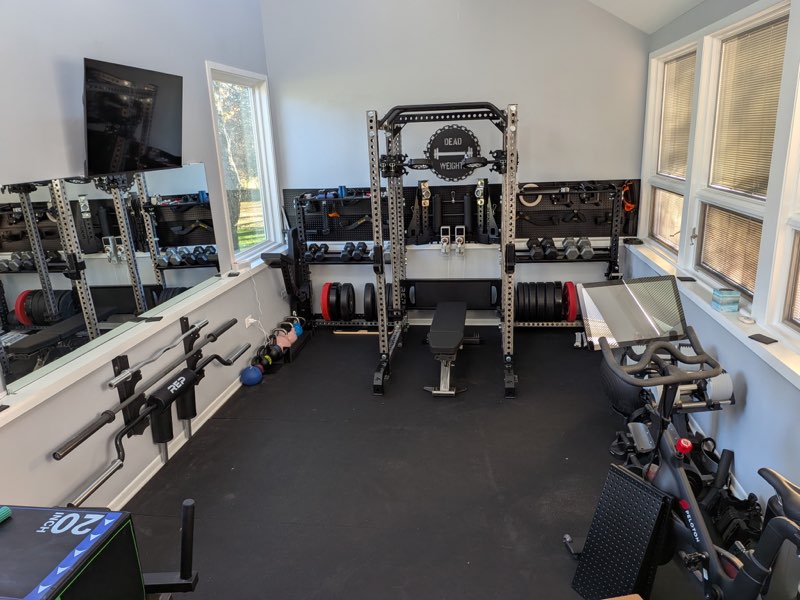 Finished home gym build with rack, storage, dumbbells, and cardio equipment